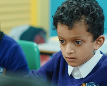 a boy is sitting at a desk with a laptop