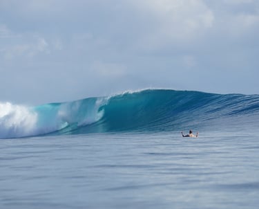 Crystal blue Mentawai wave breaking with surfer waiting in lineup