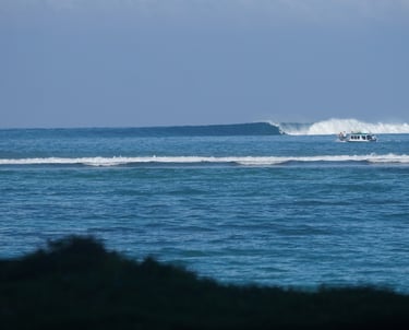 Breaking waves at Suicides surf spot near Toska with boats anchored in channel
