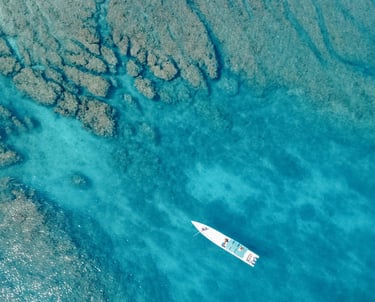 erial view of a surf boat floating above crystal-clear reef in the Mentawai Islands.
