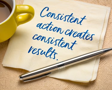 consistent action creats consistent results handwritten on a napkin amd a pen near a cup of coffee