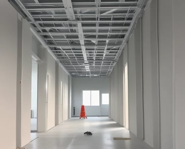 The image depicts an unfinished interior space with exposed brick walls and a concrete floor. Construction materials such as wooden boards, buckets, and other building supplies are scattered around the room. There is a partially opened doorway leading to another room, highlighting the ongoing renovation process.