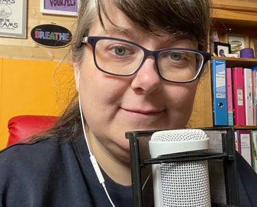 Laura Dumbleton at her recording setup with a microphone and BREATHE sign on the wall behind her