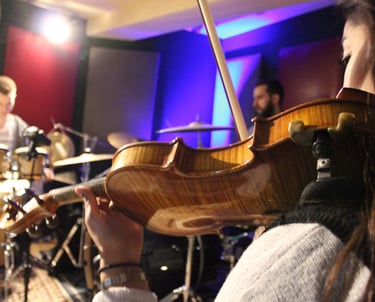 a woman playing a violin in a recording studio with a band