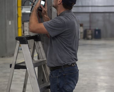 a man in a gray shirt near a ladder inspecting a maintenance tool