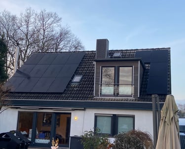 Modern house with black solar panels installed on a dark tiled roof next to a dormer window.