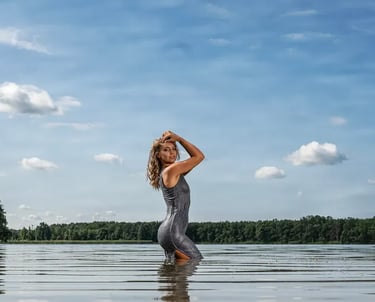 Porträt einer Frau in nassem Kleid, die kniehoch im Wasser eines Sees steht. 