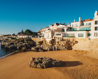 Plage de sable fin à Cascais, Portugal, avec ses maisons blanches en bord de mer sous un ciel ensole