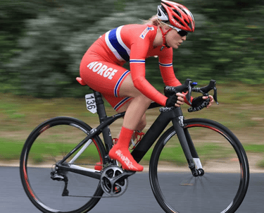 Professional female cyclist in red Norway national team kit racing on a carbon fiber road bike.