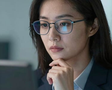 A close-up of a professional woman with glasses looking thoughtfully at a screen, illuminated by soft blue light. She represents the expert advisor team. North American / US professional setting.