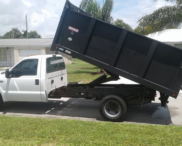 a white truck with a black dumpster sitting on the side of a driveway