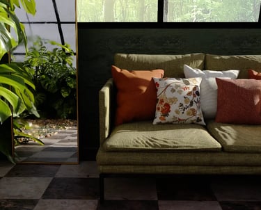 Įvairių spalvų dekoratyvinės pagalvėlės ant žalios sofos prie augalo