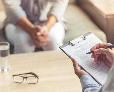 Zwei Personen in einer Psychotherapiesitzun. Der Psychotherapeut macht sich Notizen.