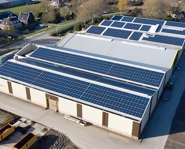Aerial view of a large commercial warehouse roof covered in solar panel installations for renewable energy.