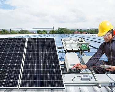 A solar technician in safety gear performs maintenance on industrial rooftop solar panels.