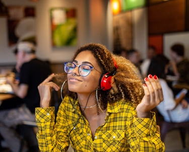 a woman in a yellow shirt with red headphones on smiling as she sits at a cafe