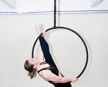 Vrouw in zwarte outfit voert een aerial hoop oefening uit bij De Polecats Fabriek in Gent