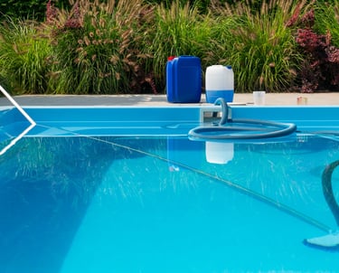 Pool cleaning hose chemical containers water testing kit beside a clear blue swimming pool.