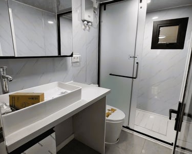 Modern white bathroom featuring a marble-patterned wall, vessel sink, and frosted glass shower door.
