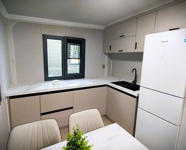 Modern minimalist kitchen with white Hisense refrigerator, marble countertops, and beige cabinets.