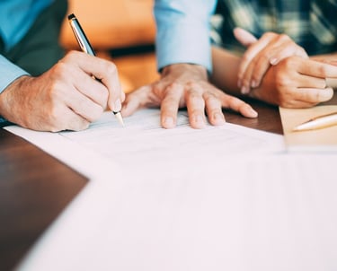 a man and woman sitting at a table with papers and pen