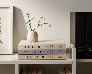 Stack of decorative books with minimalist gold foil accents styled on a bookshelf with a vase
