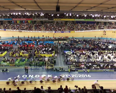 a group of people riding bicycles in a velodrome with lots of spactators