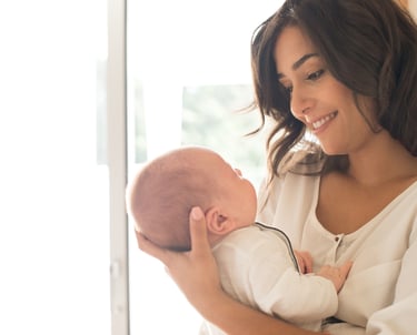 Happy mother holding her little baby in hand and looking at the baby with a smile