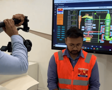 a man in a blue shirt and a camera shooting another man wearing glasses and aditya birla hindalco