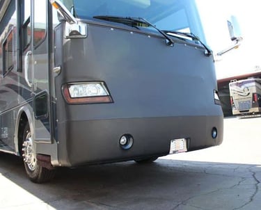 A motorhome with a black protective vinyl front mask cover parked on a paved lot.
