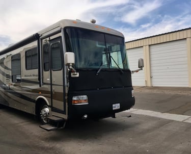 A luxury Newmar Dutch Star motorhome RV parked at a storage facility with a protective front mask cover.