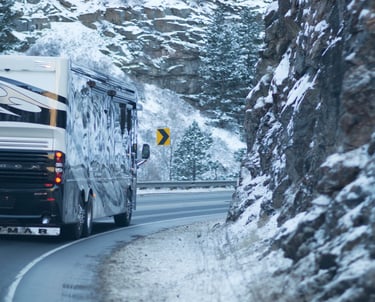 A luxury Newmar Essex motorhome RV driving on a winding snowy mountain road.