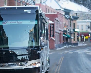 A luxury Newmar Essex motorhome driving through a snowy mountain town street with historic buildings.