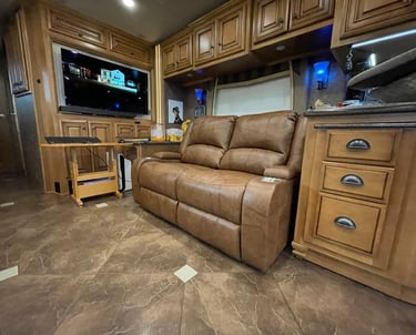 Luxurious RV interior featuring a brown leather recliner sofa, custom wood cabinets, and a flat-screen TV.