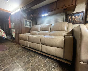 Tan leather reclining sofa in an RV living area with wood cabinets and tile flooring.
