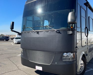 A black Class A motorhome with a protective vinyl bra cover parked in a sunny lot.