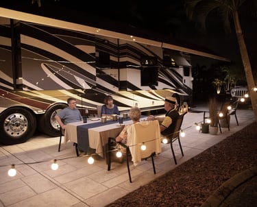 Two senior couples enjoying an outdoor dinner at night beside a luxury Class A RV motorhome.