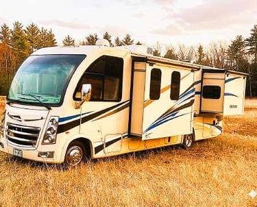 A white Class A motorhome RV parked in a field with slides extended for luxury camping.
