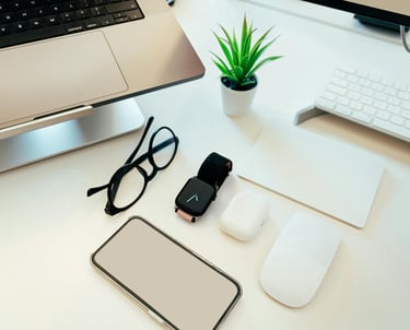 a computer monitor, keyboard, mouse, earpods, glasses, a plant showing the use of digital products