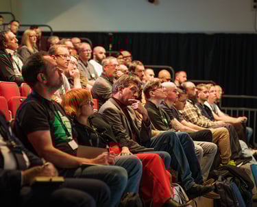 a group of people sitting in a auditorium with people watching a presentation