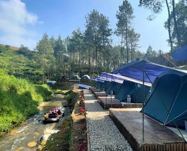 Tenda camping biru di pinggir sungai alam terbuka Pangalengan dengan pemandangan pepohonan pinus