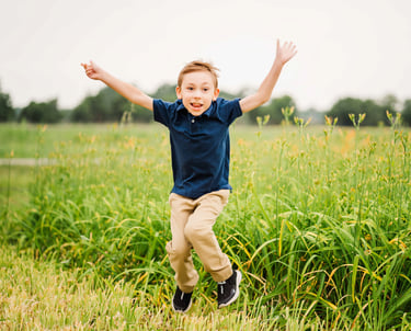 a young boy jumping in the grass with his hands up