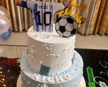 Lionel Messi themed two-tier birthday cake with soccer ball topper and Argentina jersey decoration.