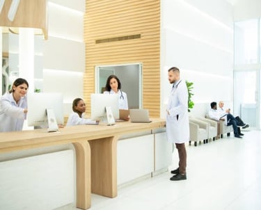 Un médico se encuentra en el mostrador de recepción de un consultorio médico, tres asistentes detrás