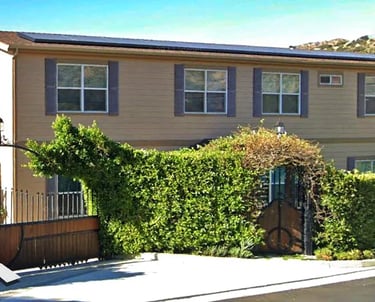 Two story modular home behind front gate and shrubs.
