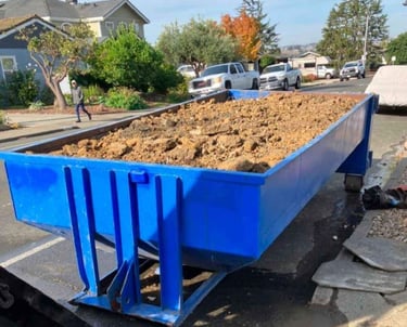 a blue dumpster truck with a large pile of dirt