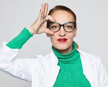 eine Therapeutin mit freundlichem Gesicht und Zopf fasst sich mit der rechten Hand an Ihre Brille ,