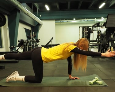 Una donna in maglia gialla esegue un esercizio di equilibrio in ginocchio, estendendo il braccio e la gamba opposti,