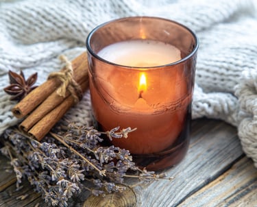a bundle of lavender, cinnamon sticks and a candle in a glass candle holder, resting on a blanket