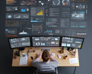 Analyst monitoring data analytics and software code on multiple computer monitors in a workstation.